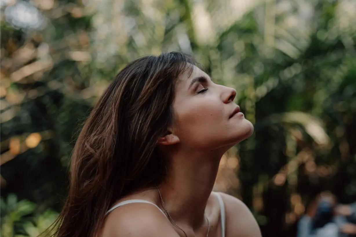 Close up upper body profile shot of a beautiful happy young Caucasian woman enjoying the tropical atmosphere with her eyes closed surrounded by palm trees in a tropical public park.