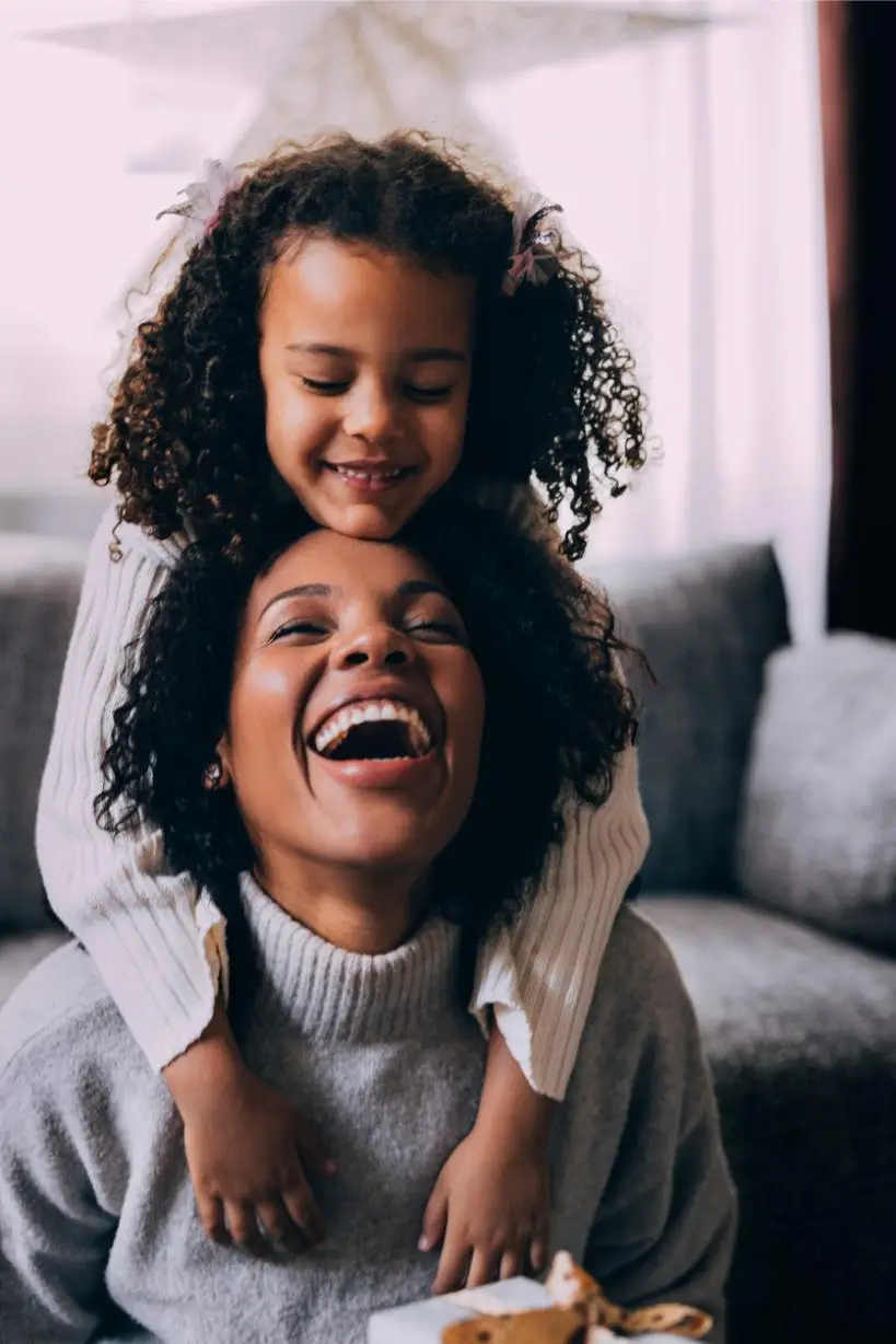 Little Cuban daughter hugging her mother from behind.